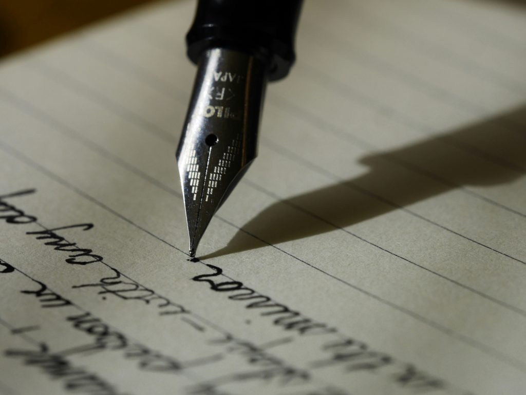 Image shows nib of pen writing on lined paper