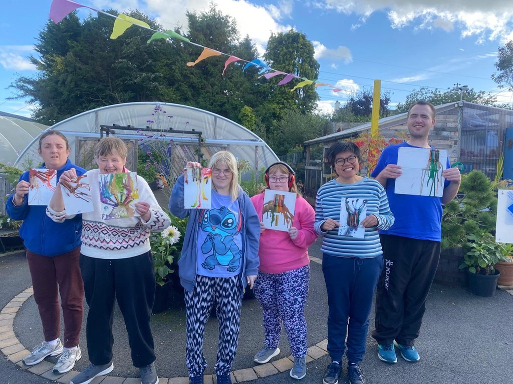 6 children holding up drawings. There is a poly tunnel in the background and bunting above them.